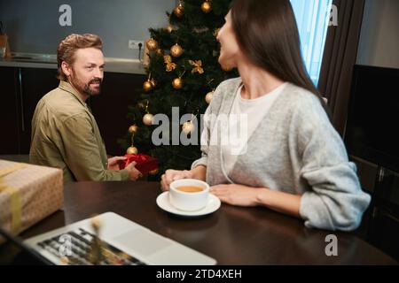 Mann mit Geschenkbox und Frau mit einer Tasse Kaffee, die sich auf den Neujahrsferien vorbereitet Stockfoto