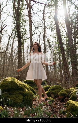 Schneeglöckchen galanthus-Frau. Sie steht in einem weißen Kleid auf einer Wiese mit Schneeglöckchen in einem Frühlingswald Stockfoto