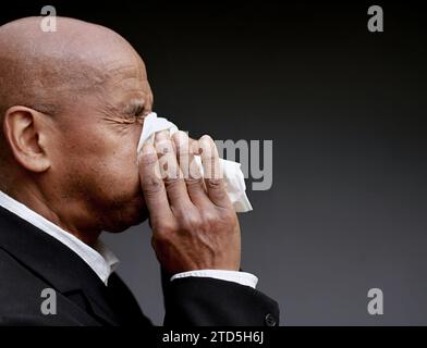 Mann, der die Erkältung und Grippe fängt Mann, der Nase bläst, nachdem er eine Erkältung mit grauem Hintergrund mit Leuten Stock Foto gefangen hat Stockfoto