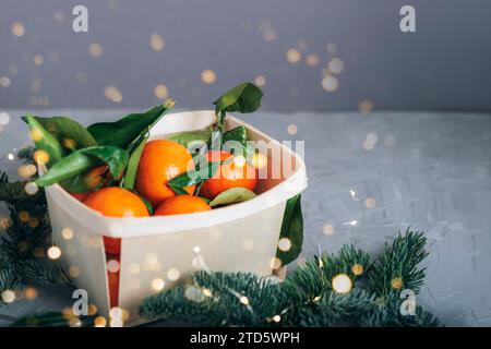 Mandarinen in einem Korb mit weihnachtslichtern auf grauem Hintergrund. Stockfoto