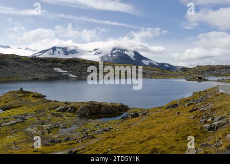 Der See ist umgeben von schneebedeckten Bergen unter blauem Himmel mit einigen weißen Wolken in Norwegen. Stockfoto