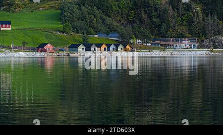 Farbenfrohe Gebäude entlang der Hügelseite und ihre Reflexionen auf dem See in Sogndal, Norwegen. Stockfoto