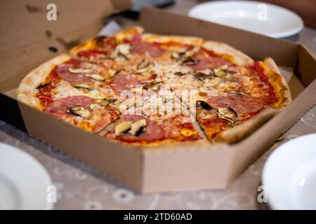 Große Pizza in Stücke geschnitten in einer Kiste auf dem Tisch. Essen nach Hause bestellen. Stockfoto