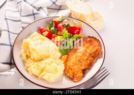 Gebratenes Hähnchensteak oder Schnitzel mit Kartoffelpüree und Gemüsesalat auf einem Teller auf weißem Tisch Stockfoto
