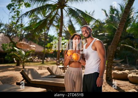 Glückliches Paar genießt tropisches Resort, Mann und Frau halten Kokosnussgetränk. Romantischer Flitterwochenurlaub, Entspannung am Strand, Liebe. Sonnenküsste Duo Lächeln Stockfoto