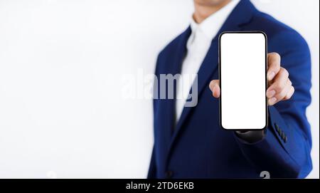 Geschäftsmann Hand hält mobiles weißes leeres Display, Mock Up Handy Handy im Anzug hält Handy mit leerem weißen Bildschirm auf dunkelblauem B Stockfoto
