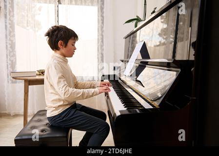 Der hübsche Teenager-Pianist spielt Klavier und singt drinnen. Der talentierte Teenager-Musiker kreiert Musik und Lied, spielt auf dem Klavier, komponiert einen melo Stockfoto