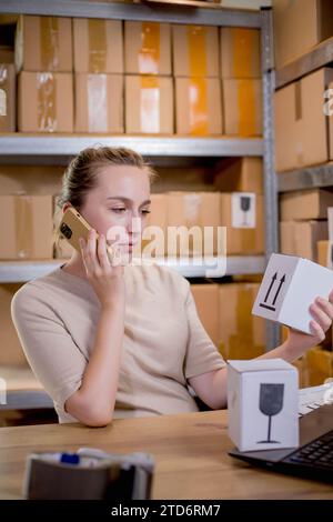 Frau, die ein Mobiltelefon oder Tablet verwendet, um mit Kunden zu kommunizieren. Lieferung von Waren über private Kurierdienste. Konzepte des Online-Verkaufs und weiter Stockfoto