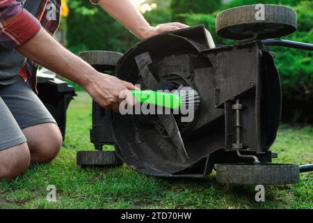 Mann, der den Rasenmäher mit Bürste im Garten reinigt, Nahaufnahme Stockfoto