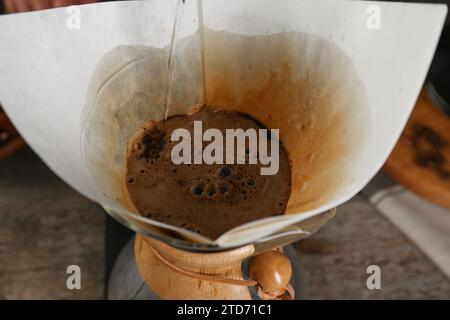 Heißes Wasser in eine chemex-Glaskaffeemaschine mit Papierfilter am Tisch, Nahaufnahme Stockfoto