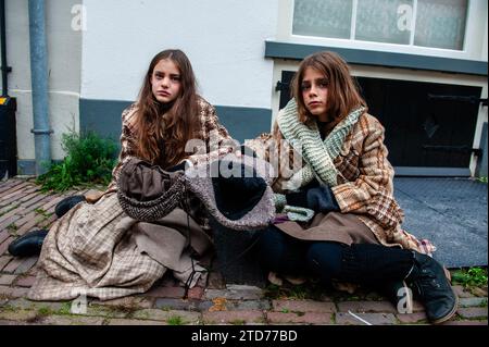 Deventer, Niederlande . Dezember 2023. Zwei kleine Mädchen sitzen auf dem Boden und treten als Obdachlose auf. Jedes Jahr, um dieses Datum, lebt die Welt des englischen Schriftstellers Charles Dickens aus dem 19. Jahrhundert in der schönen niederländischen Stadt Deventer wieder. Mehr als 950 Charaktere aus den berühmten Büchern von Dickens zurück ins Leben. Wohlhabende Damen und Herren mit Spitzhüten ziehen durch die Straßen. Die Landschaft des Festivals besteht aus historischen Gebäuden, Weihnachtsbäumen und Tausenden von kleinen Lichtern. Quelle: SOPA Images Limited/Alamy Live News Stockfoto