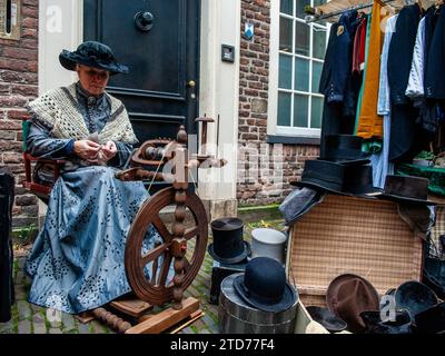 Deventer, Niederlande . Dezember 2023. Eine Frau zeigt die Arbeit des traditionellen Spinnens. Jedes Jahr, um dieses Datum, lebt die Welt des englischen Schriftstellers Charles Dickens aus dem 19. Jahrhundert in der schönen niederländischen Stadt Deventer wieder. Mehr als 950 Charaktere aus den berühmten Büchern von Dickens zurück ins Leben. Wohlhabende Damen und Herren mit Spitzhüten ziehen durch die Straßen. Die Landschaft des Festivals besteht aus historischen Gebäuden, Weihnachtsbäumen und Tausenden von kleinen Lichtern. Quelle: SOPA Images Limited/Alamy Live News Stockfoto