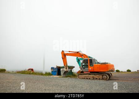 Ein orangefarbener geparkter großer Bagger, ein Bauwagen, schwere Erdbewegungsmaschinen an bewölkten Tagen Stockfoto