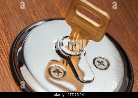 Ein gelber Messingschlüssel wird in ein Zylinderschloss gesteckt. Makrofotografie Stockfoto