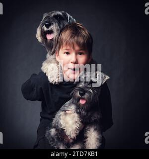 Porträt eines Kindes mit Miniatur-Schnauzer-Welpen. Studio auf dunklem Hintergrund. Stockfoto