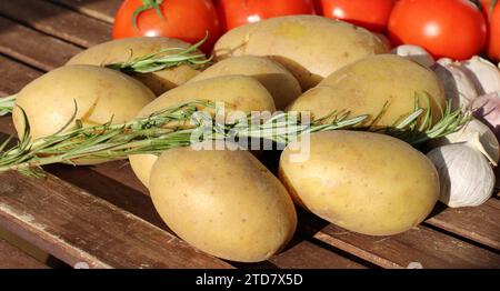 Österreichische Kartoffeln mit Rosmarin-Tomaten und Knoblauch auf einem Holztisch bei Sonnenschein - frische Zutaten für verschiedene Kartoffeltomaten-Gerichte Stockfoto