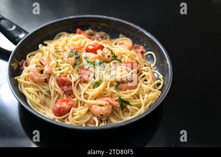 Spaghetti mit Garnelen, Tomaten und Kräutern, schwarze Pfanne auf dem Herd, Kochen einer mediterranen Meeresfrüchtemahlzeit, Kopierraum, ausgewählter Fokus, Kommentar Stockfoto