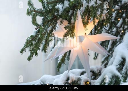 Beleuchteter weißer Mährischer Stern hängt in einer schneebedeckten Weihnachtstanne als festliche Weihnachtsdekoration, Kopierraum, sele Stockfoto