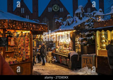 Lübeck, 6. Dezember 2023: Beleuchtete Verkaufsstände mit Schnee auf den Dächern auf dem Weihnachtsmarkt in der historischen Altstadt von Lübeck, Kopie Stockfoto