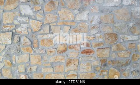 Strukturierte Zementwand mit verschiedenen rauen, unregelmäßigen Steinen in Grau, Beige und Ocker. Ideal für Hintergründe Stockfoto