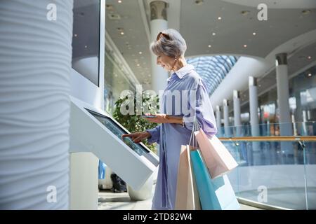 Ältere Frau, die geldautomaten benutzt, um Geld im Einkaufszentrum abzuheben Stockfoto