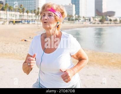 Alte Dame, die am Strand läuft Stockfoto