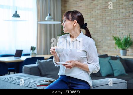 Entspannte Frau mittleren Alters mit einer Tasse Kaffee auf dem Sofa im Wohnzimmer Stockfoto