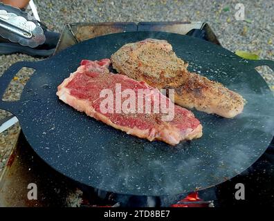Steaks auf dem Campingplatz kochen. Braten Sie Steaks in einer Pfanne auf dem Campingplatz. Steaks in einer Pfanne. Zwei fette saftige Steaks in Olivenöl in einer Pfanne gebraten. Stockfoto