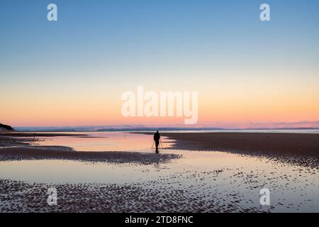 Fotograf mit Stativ, der bei Ebbe die Winterdämmerung über Findhorn Beach ansieht. Findhorn, Morayshire, Schottland. Stockfoto