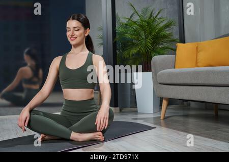 Achtsame junge Frau, die Stressentlastungsmeditation in Sukhasana-Pose praktiziert. Stockfoto