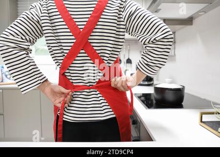 Rückansicht einer Frau, die Essen zubereitete, während sie ihre Schürze in der Küche bindet Stockfoto