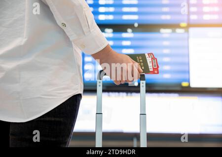 Frau, die auf die Flugzeitinformationstafel am Flughafen blickt und Pass und Ticket in der Hand Stockfoto