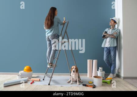 Ein junges Paar mit Beagle-Hund, der in der Nähe der blauen Wand in ihrem neuen Haus repariert Stockfoto