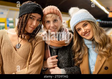 Drei fröhliche junge Frauen in lässiger Wintermode posieren für ein Foto in einer U-Bahn-Station, die Freundschaft und Freude ausstrahlen. Stockfoto