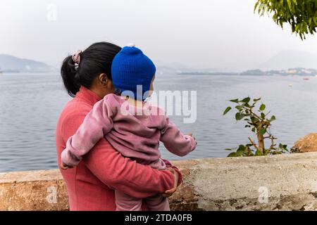 Die junge Mutter mit ihrem Sohn, die am Morgen die Bergsee-Landschaft betrachtet, wird im Jagdish-Tempel udaipur rajasthan indien aufgenommen. Stockfoto