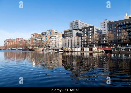Amsterdam Niederlande 17. Dezember 2023 vergleichsweise moderne Wohnhäuser spiegeln sich an einem Wintertag mit azurblauem Himmel im Wasser Westerdoks wider. Stockfoto