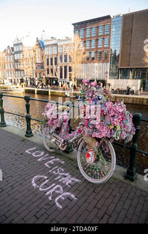 Amsterdam Niederlande 17. Dezember 2023 Anne Frank Haus an der Prinsengracht. Auf dem Kanal vor der Tür steht ein farbenfroh verziertes rosafarbenes Fahrrad mit der Botschaft. Liebe ist das Heilmittel Anne Frankhuis, versierde, fiets, Rose, Stockfoto