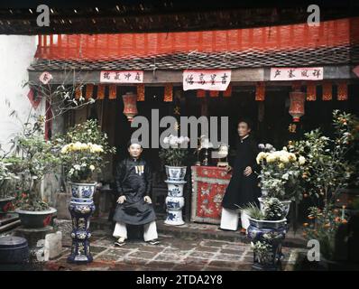 Hà-nôi, Hainoi Vietnam, Tonkin, Indochina zwei prominente Persönlichkeiten vor dem Altar der Ahnen im Innenhof eines wohlhabenden Hauses, dekoriert mit Chrysanthemen, zur Zeit des Têt Festivals, Festivals, Kleidung, Religion, Menschen, Habitat, Architektur, Inschrift, Information, Volksfest, Kostüm, Neujahr, Ahnenverehrung, Lampion, Chrysantheme, Porträt, Altar, Vase, Wohnung, religiöse Inschrift oder Votivinschrift, Möbel, Blume, Keramik, Medaille, Dekoration, Frisur, Kopfbedeckung, Innenhof, Raucher, Mann, Indochina, Tonkin, Hanoi, Hof desselben Hauses in Hanoi beim tim Stockfoto