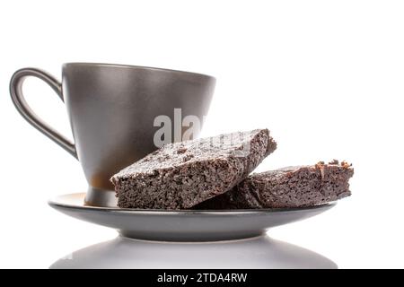 Zwei Stücke klassischer Schokoladenbrownie auf Keramikuntertasse mit schwarzer Tasse, Makro, isoliert auf weißem Hintergrund. Stockfoto