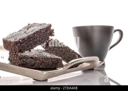 Drei Stücke klassischer Schokoladenbrownie auf Metalltablett mit Keramikbecher, Makro, isoliert auf weißem Hintergrund. Stockfoto