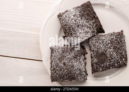 Drei Stücke klassischer Schokoladenbrownie mit Keramikuntertasse auf Holztisch, Makro, Blick von oben. Stockfoto