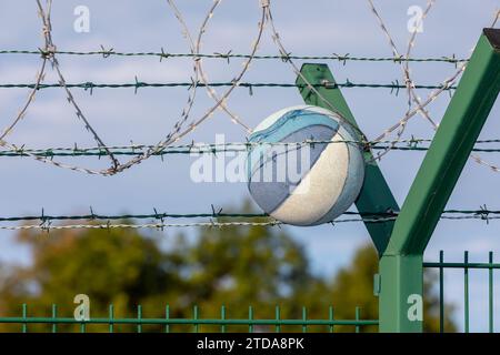 Alter, verlassener Basketball, gefangen in Barb Draht an der Grenze, verschwommener Baumhintergrund, Sicherheitszaun Stockfoto