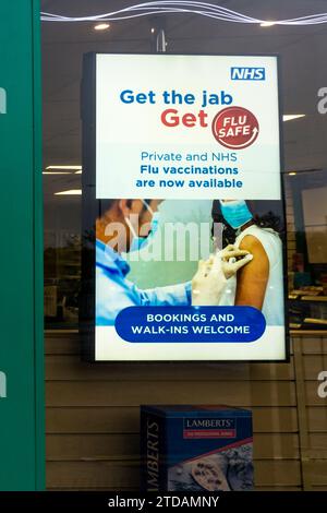 Ein NHS-Schild in einem Apothekenfenster ermutigt Menschen, einen Grippejab zu haben. Stockfoto