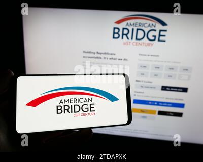 Person, die ein Smartphone mit dem Logo der liberalen Super PAC American Bridge 21st Century vor der Website hält. Schwerpunkt auf dem Display des Telefons. Stockfoto