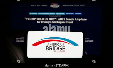 Person mit Handy mit Logo der liberalen Super PAC American Bridge 21. Jahrhundert vor der Webseite. Schwerpunkt auf dem Display des Telefons. Stockfoto