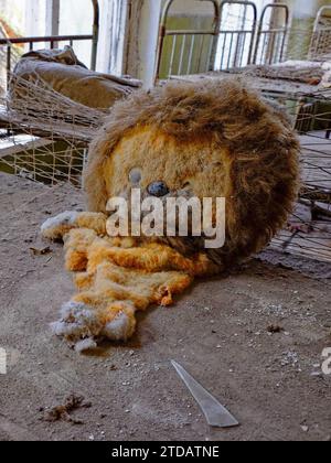 Ein gefülltes Löwenspielzeug. Ein altes, zerrissenes Plüschtier in einem verlassenen Kindergarten. Ein verlassener Kindergarten in Tschernobyl. Stockfoto