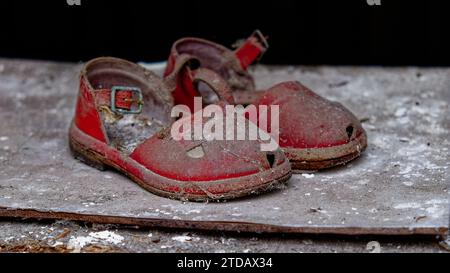 Ein paar alte, rote Sandalen, die mit Staub bedeckt sind, werden auf einer grauen Oberfläche abgelegt. Stockfoto