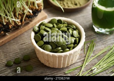 Trockene Tabletten mit grünem Gerstengras, reich an Chlorophyll, mit frisch angebauten Klingen und Saft im Hintergrund Stockfoto