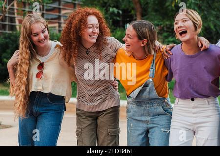 Eine Gruppe fröhlicher Studentinnen in lässiger Kleidung, die lachen und ein schönes Wochenende genießen. Echte coole Mädchen, die sich mit einem Zahnlächeln umarmen. Glückliche Freundinnen, die draußen Spaß haben. Hochwertige Fotos Stockfoto