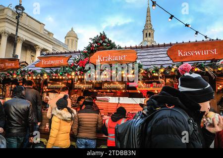 London, Großbritannien. Dezember 2023. In einem deutschen Würstelstand stehen Menschen trotz relativ hoher Preise für Essen an. Der Weihnachtsmarkt vor der National Gallery am Trafalgar Square erweist sich als beliebt bei den Massen von Touristen und lokalen Besuchern, die Snacks, heiße Getränke und handwerkliche Weihnachtsgeschenke suchen. Quelle: Imageplotter/Alamy Live News Stockfoto